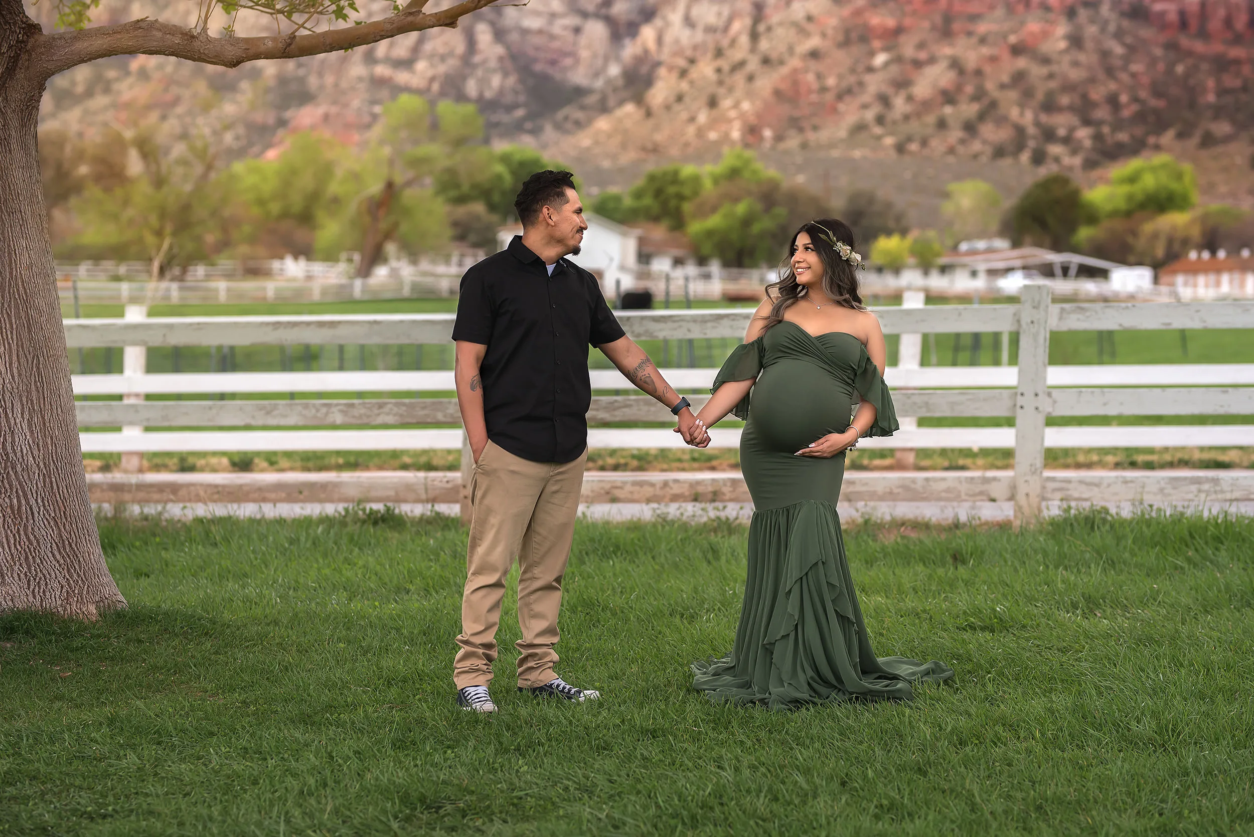 couple holds hands by white fence at Spring Mountain Ranch while mother holds baby bump