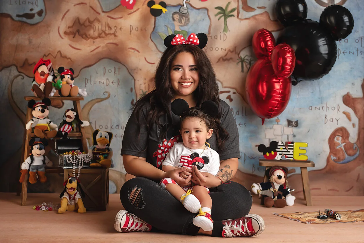 mom sits with son during Disney inspired first birthday cake smash