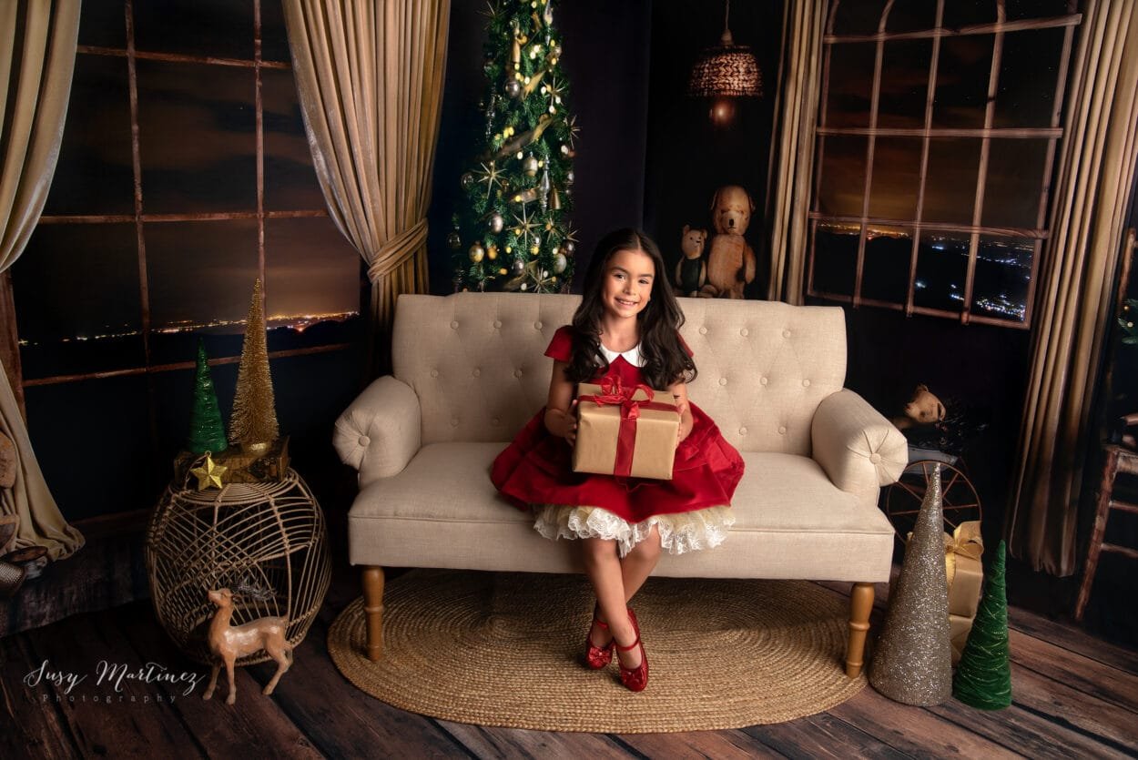 girl holding christmas gift in a golden holiday living room