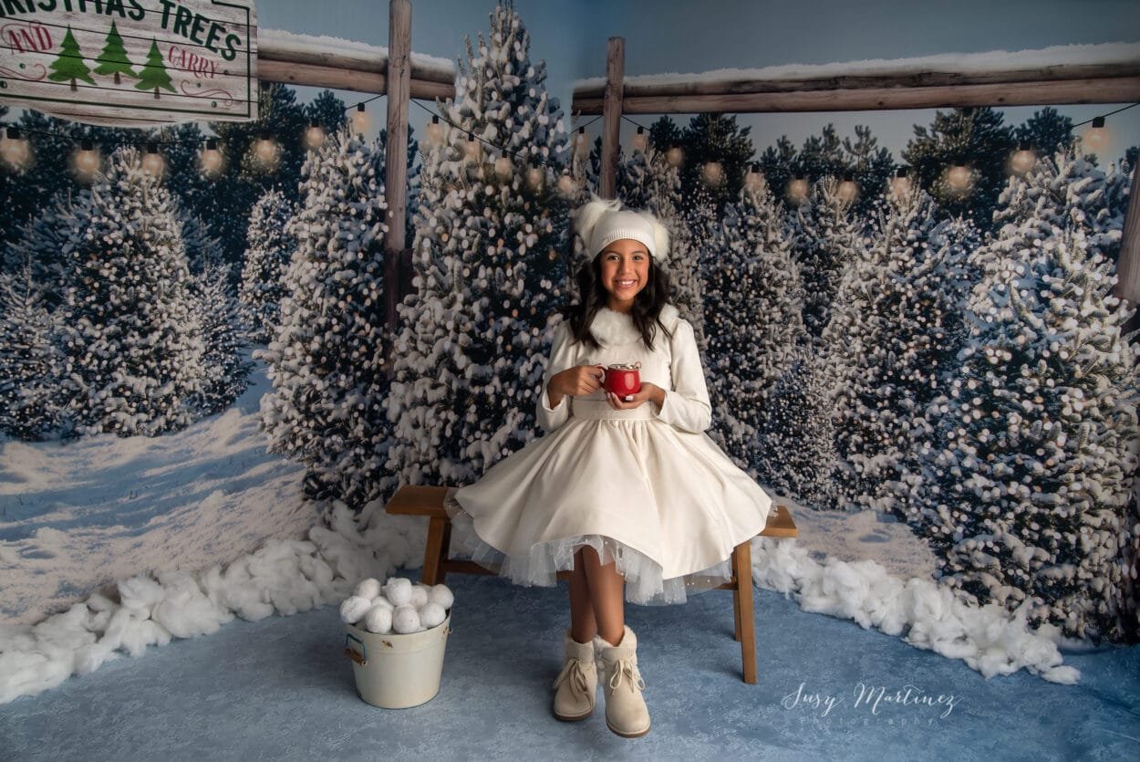 Girl drinking hot cocoa on a setting with snowy christmas trees