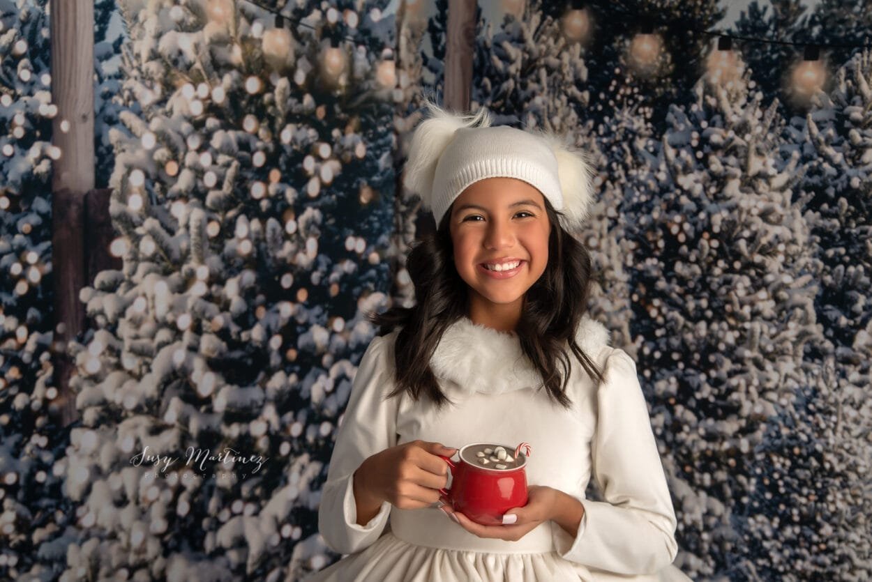 Girl holding hot cocoa mug with snowy trees behind her